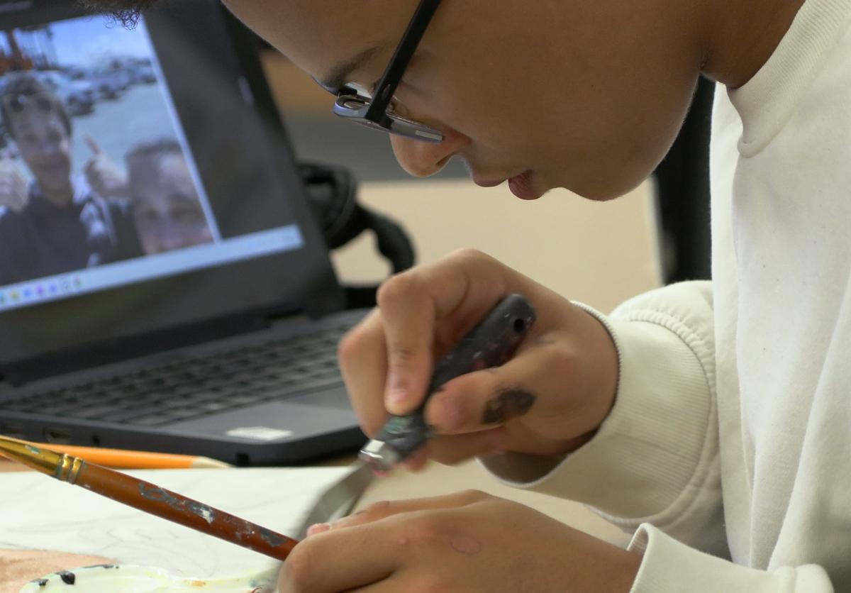 High schooler Xavier King leans close to a portrait he's painting next to his laptop.